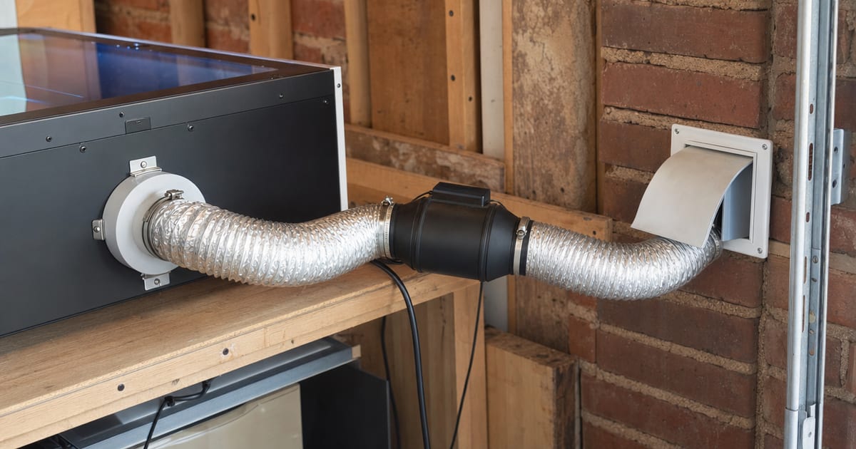 Ducting running from a laser enclosure to an outside wall vent in a garage.